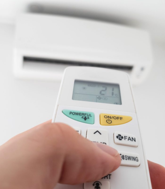 Modern airconditioner unit with a hand holding a remote.
